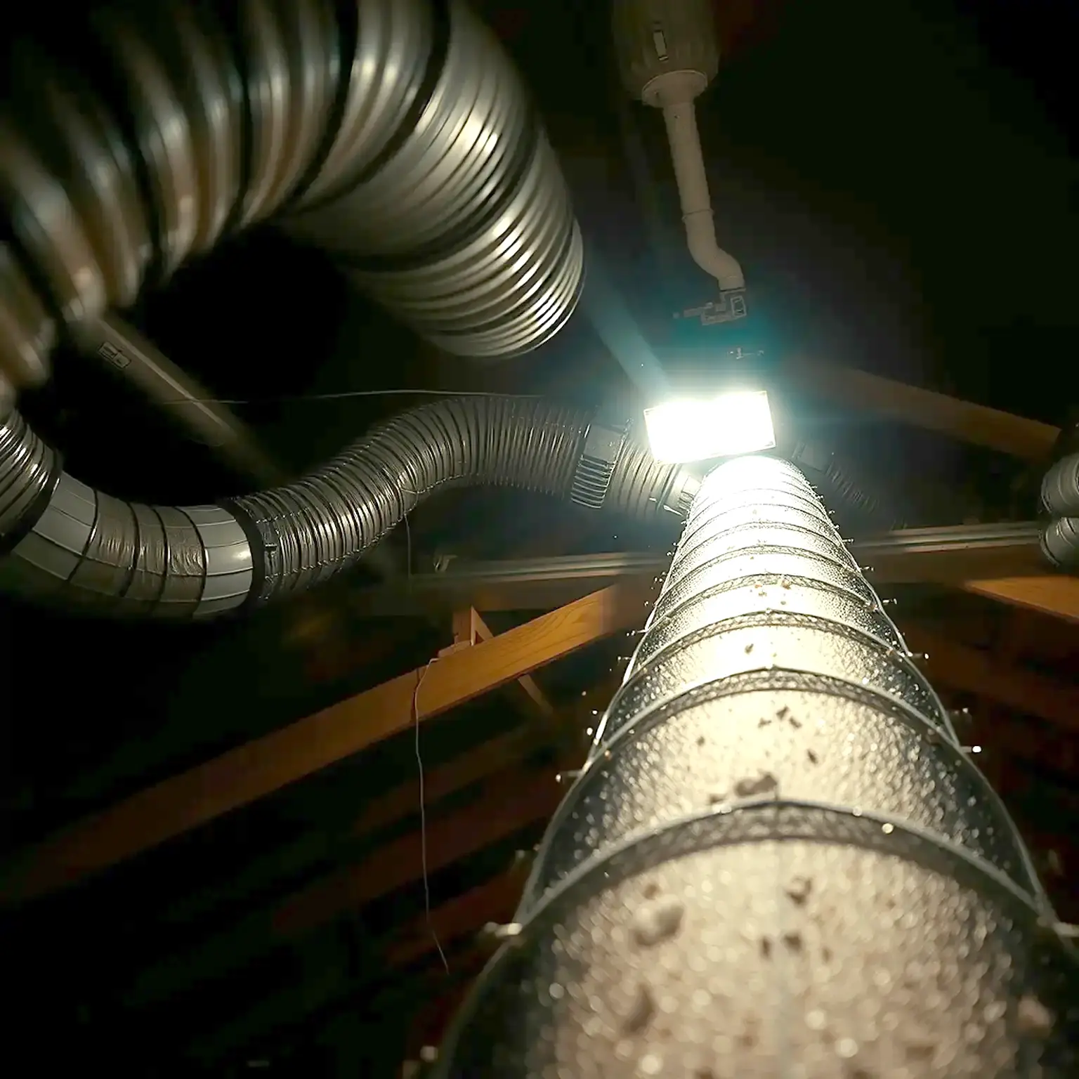 Flexible HVAC ductwork running through a dim residential attic